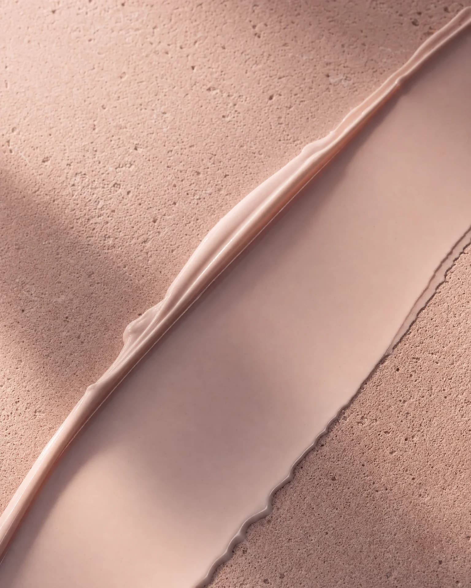 A swipe of body cream across a rough pink stone surface, leaving it smooth and polished where it has passed