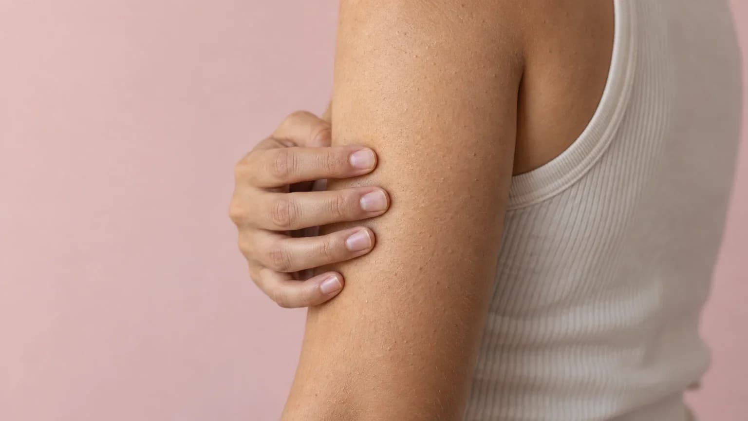 Fingertips resting on the back of a bare upper arm, checking the skin's texture by touch